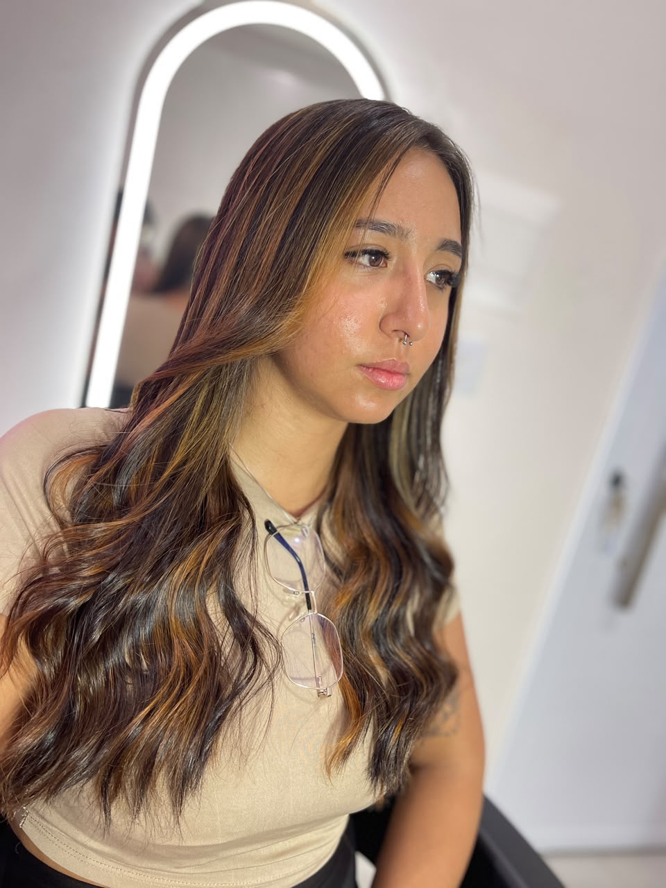 Cliente com cabelo iluminado em tons mel, em frente ao espelho do studio